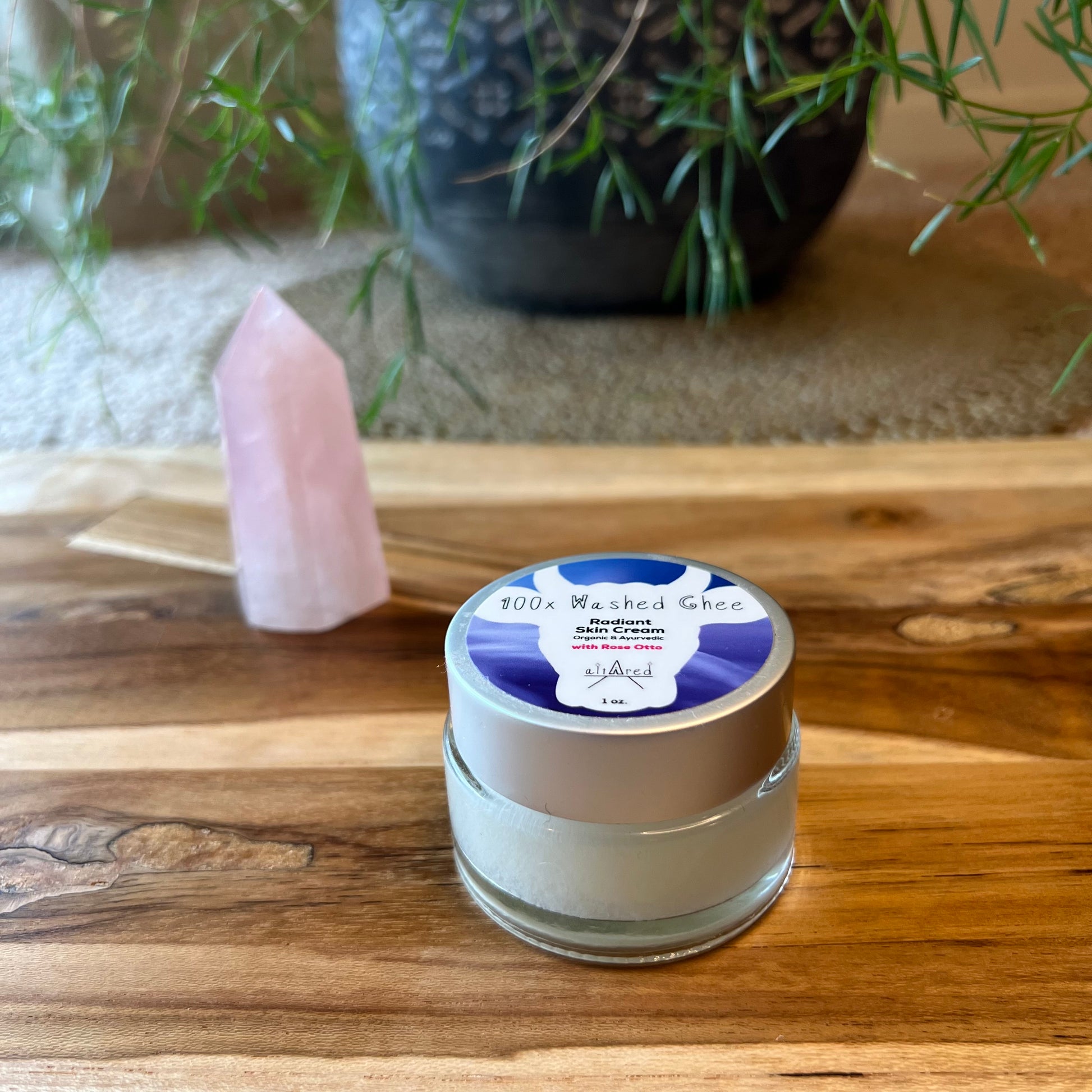 1 oz. clear glass jar of 100x Washed Ghee (Shata Dhauta Ghrita) with Rose Otto essential oil. It sits on a wooden board with a rose quartz crystal.