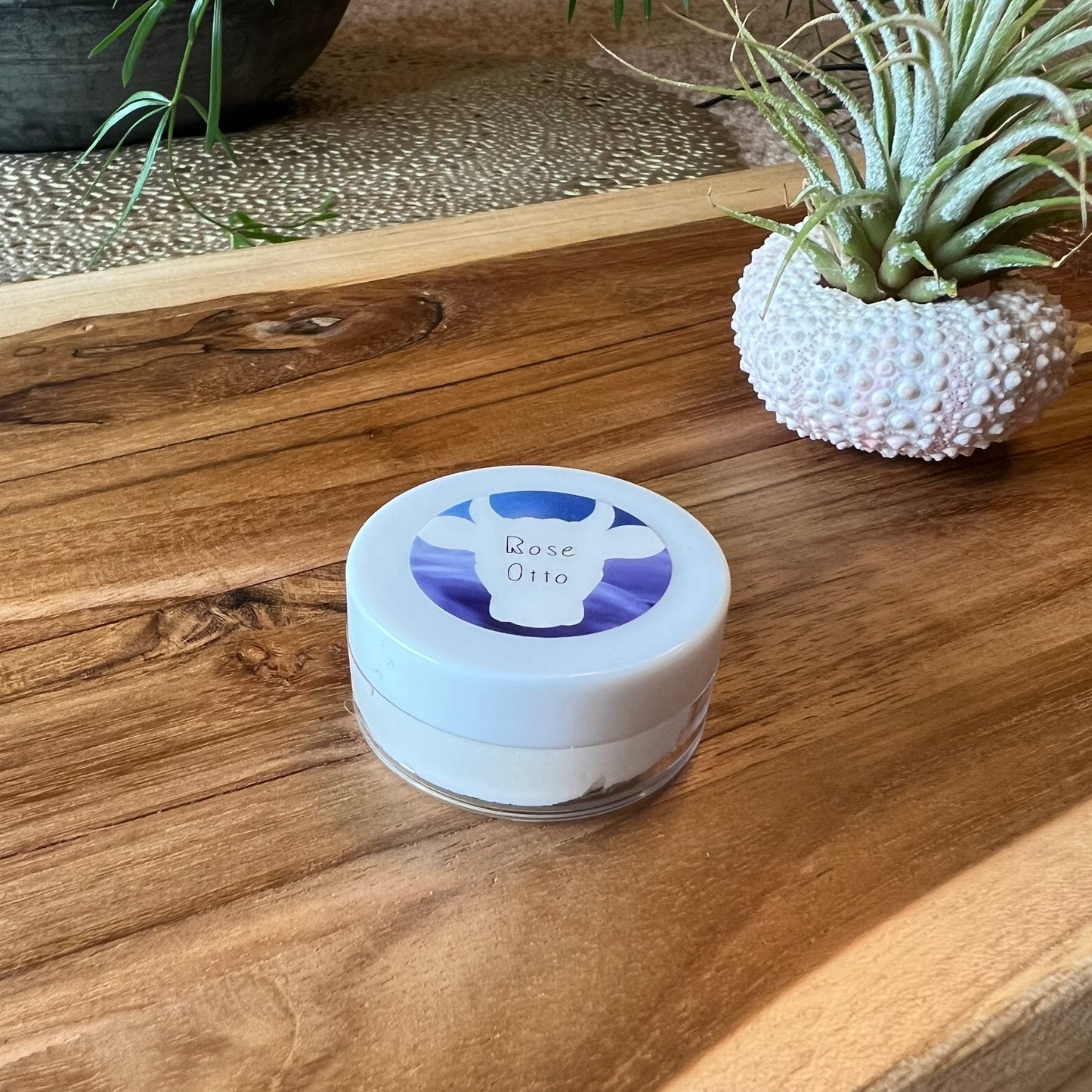 : Sample size 0.25 oz of 100x Washed Ghee Ayurvedic Skin Cream with Rose Otto essential oil sitting on a wooden board.