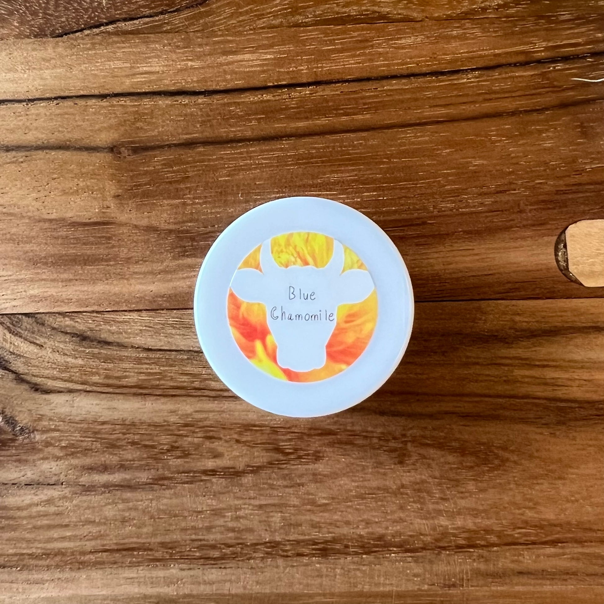 View looking straight down on a 0.25oz sample jar of 100x Washed Ghee Ayurvedic Skin Cream with German Chamomile essential oil (Shata Dhauta Ghrita), with a yellow label, on a wooden table.