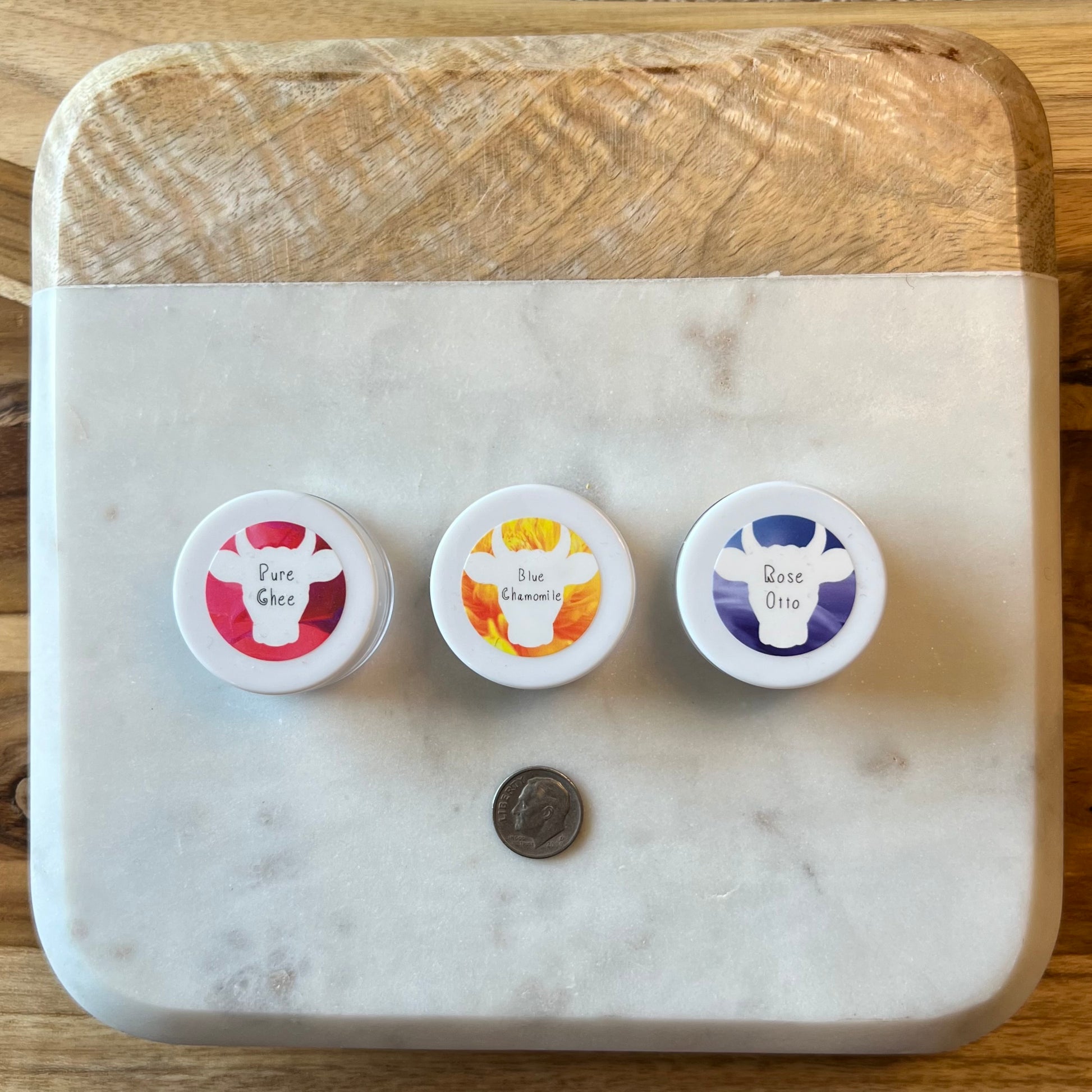 All three types of 100x Washed Ghee Ayurvedic Skin Cream sample sizes are in a row, left to right, on a marble cutting board with a dime below for size comparison.