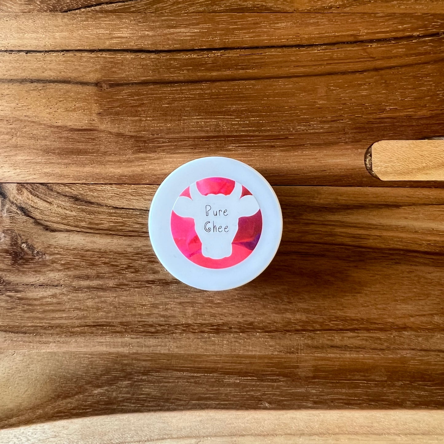 Sample size of 100x Washed Ghee Ayurvedic Skin Cream with a pink label on a wooden board.